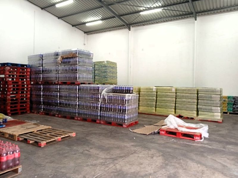 A functional industrial warehouse space featuring high ceilings with exposed steel trusses, concrete flooring, and overhead fluorescent lighting, currently utilized for storage.