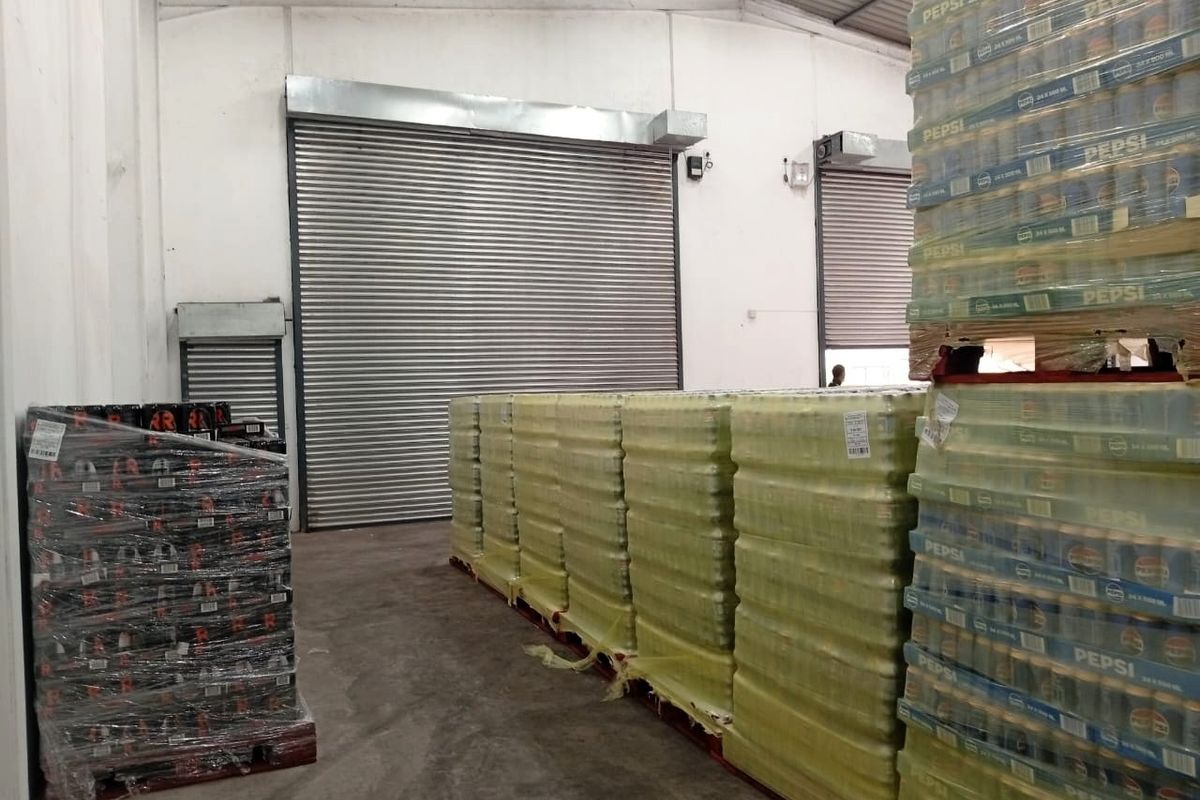 Industrial warehouse space featuring high ceilings with exposed steel trusses, concrete flooring, and multiple roller shutter doors for efficient loading and access.