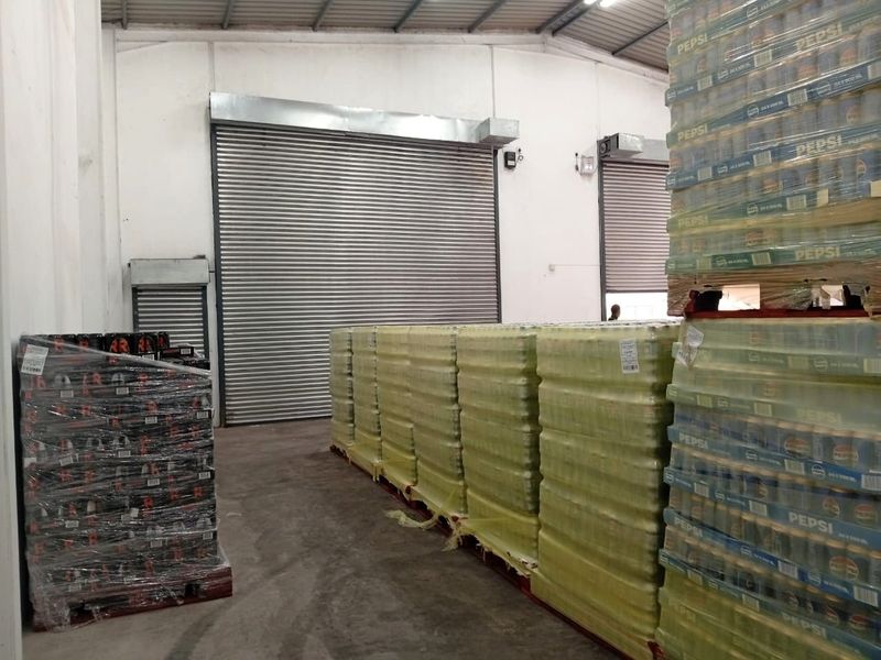 Industrial warehouse space featuring high ceilings with exposed steel trusses, concrete flooring, and multiple roller shutter doors for efficient loading and access.