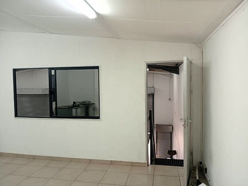 An empty industrial office space featuring tiled flooring, fluorescent lighting, and direct access to a staircase.