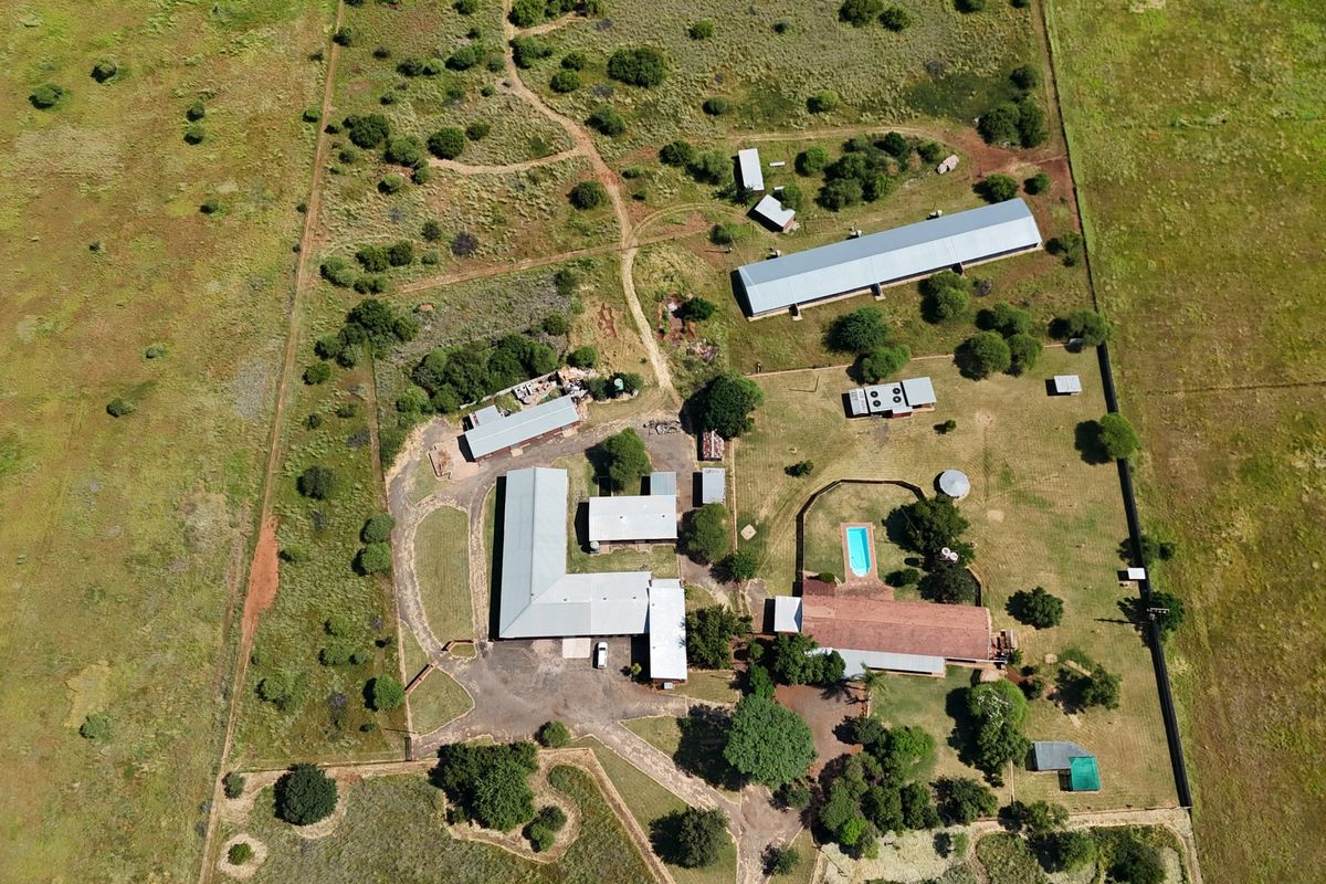 Aerial view of a small holding property featuring multiple outbuildings, a swimming pool, and extensive open land with established fencing and gravel access paths.
