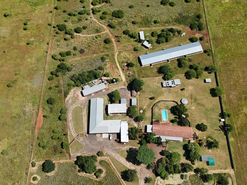 Aerial view of a small holding property featuring multiple outbuildings, a swimming pool, and extensive open land with established fencing and gravel access paths.