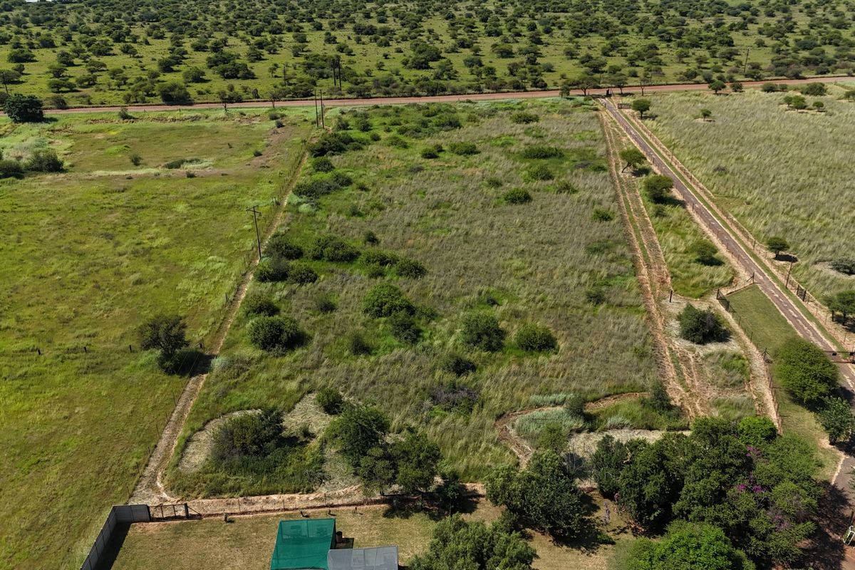 Aerial view of a large, undeveloped small holding plot featuring natural vegetation, perimeter fencing, and access road infrastructure.