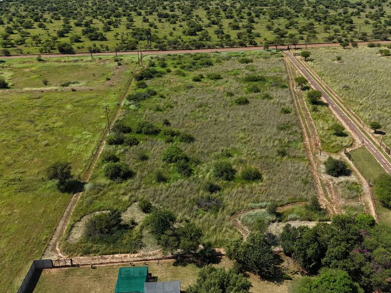 Aerial view of a large, undeveloped small holding plot featuring natural vegetation, perimeter fencing, and access road infrastructure.