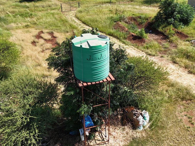 Aerial view of a small holding property featuring a green water storage tank mounted on a metal stand amidst open land.