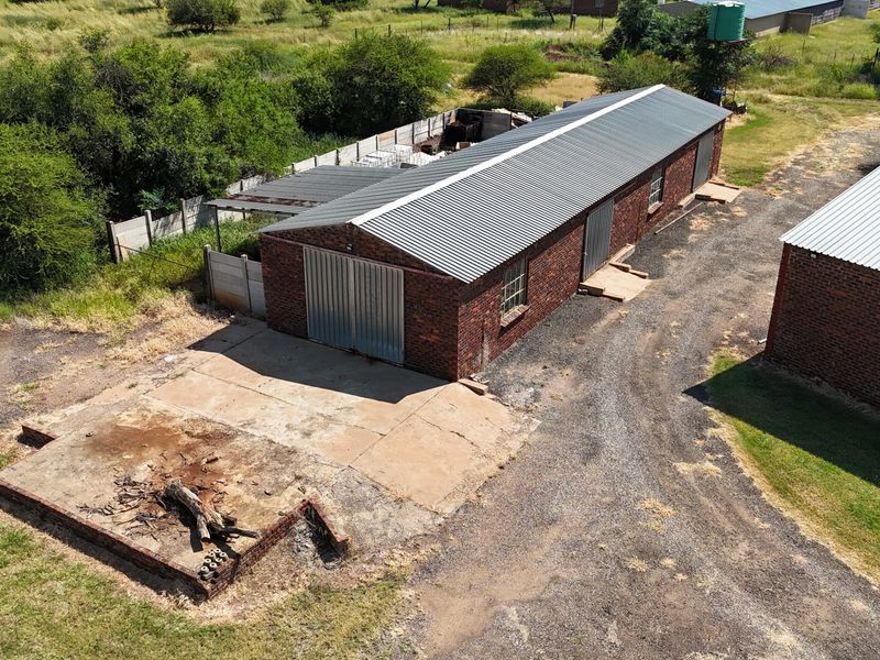 Aerial view of a brick outbuilding on a small holding, featuring a corrugated metal roof, metal doors, and an adjacent concrete apron.