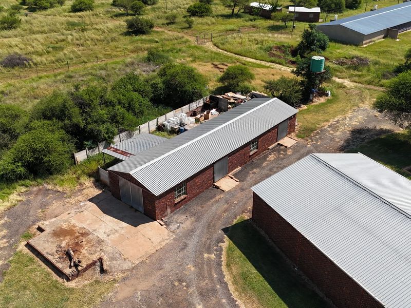 Aerial view of a small holding property featuring multiple brick outbuildings with corrugated metal roofs, a water tank, and surrounding rural land.