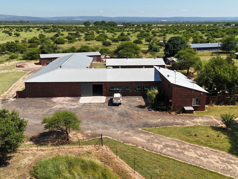 Aerial view of a large face brick small holding property featuring extensive corrugated metal roofing and a spacious gravel driveway area.