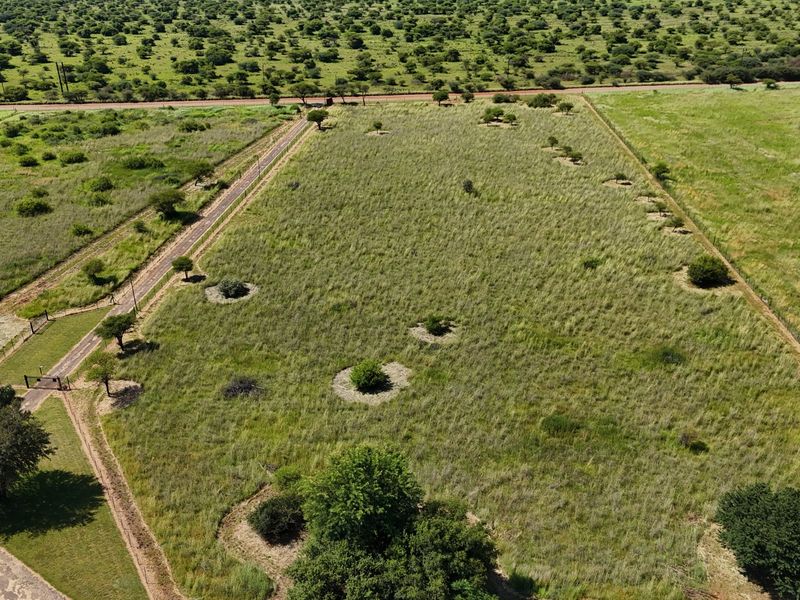 Aerial view of a large, undeveloped small holding plot featuring natural grassland, perimeter fencing, and access road frontage.