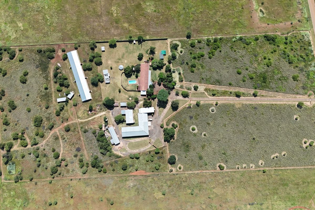 Aerial view of a large small holding property featuring multiple outbuildings, a swimming pool, and extensive open land with perimeter fencing.