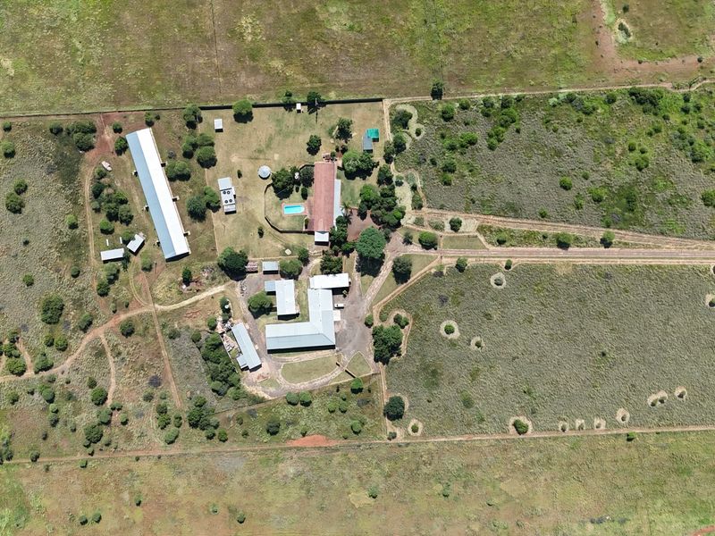 Aerial view of a large small holding property featuring multiple outbuildings, a swimming pool, and extensive open land with perimeter fencing.