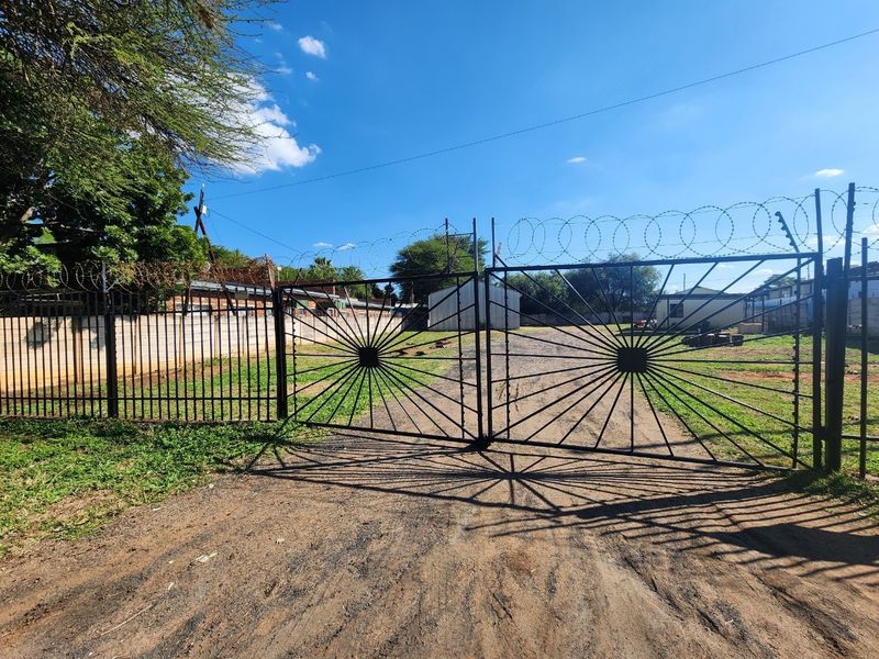 Industrial property entrance featuring a large metal security gate, perimeter walling, and razor wire fencing, providing secure access to the site.