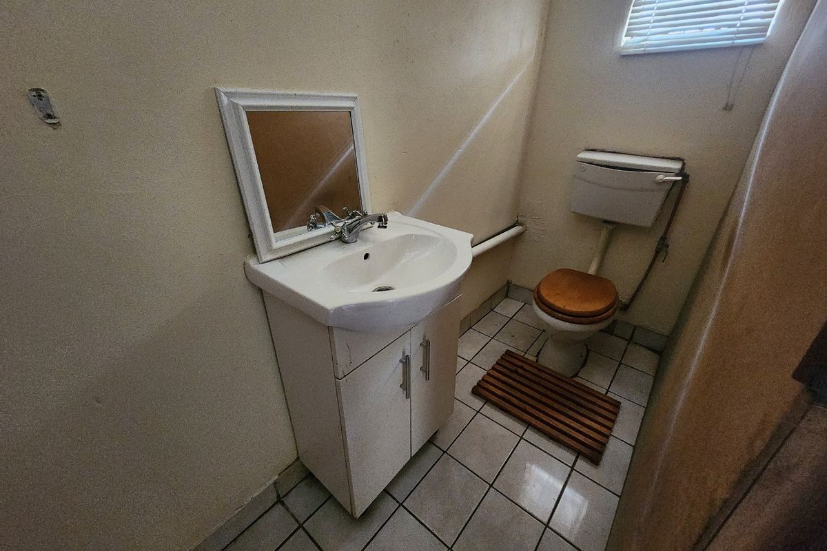 A compact bathroom featuring a vanity basin, toilet, and tiled flooring, requiring cosmetic updates to improve its overall condition and appeal.