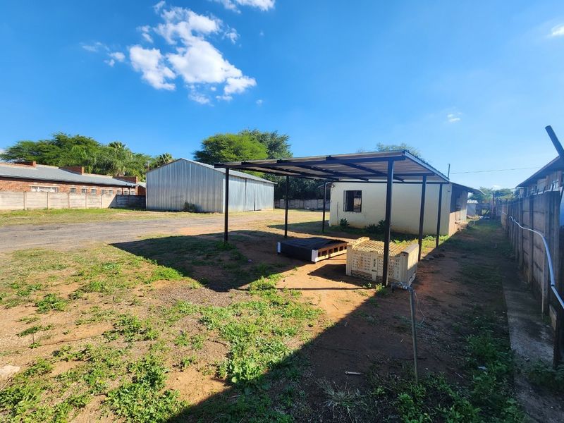 Rear industrial yard featuring a metal carport structure, a large corrugated metal storage shed, and perimeter walling.