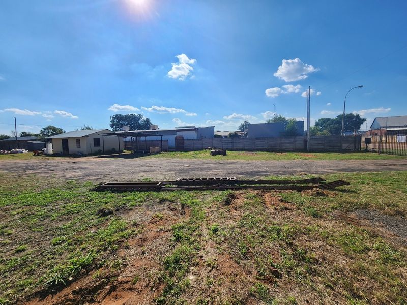 A wide view of the industrial property's rear yard, featuring a large unpaved area, boundary wall, and perimeter fencing.