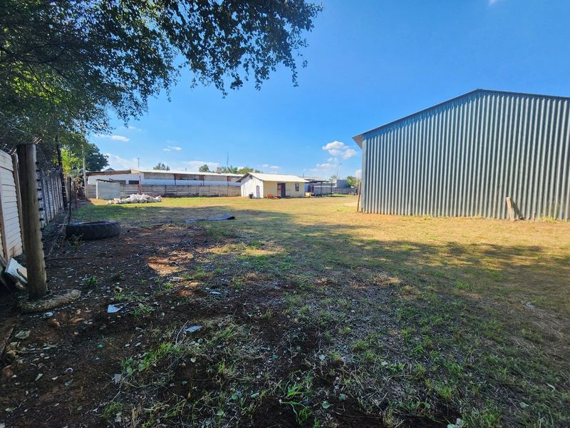 Spacious industrial rear yard featuring a large corrugated metal warehouse, perimeter electric fencing, and concrete boundary walls.