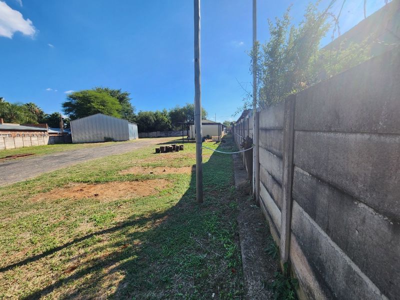 Spacious industrial rear yard featuring a precast concrete boundary wall, metal storage shed, and open gravel and grass area.