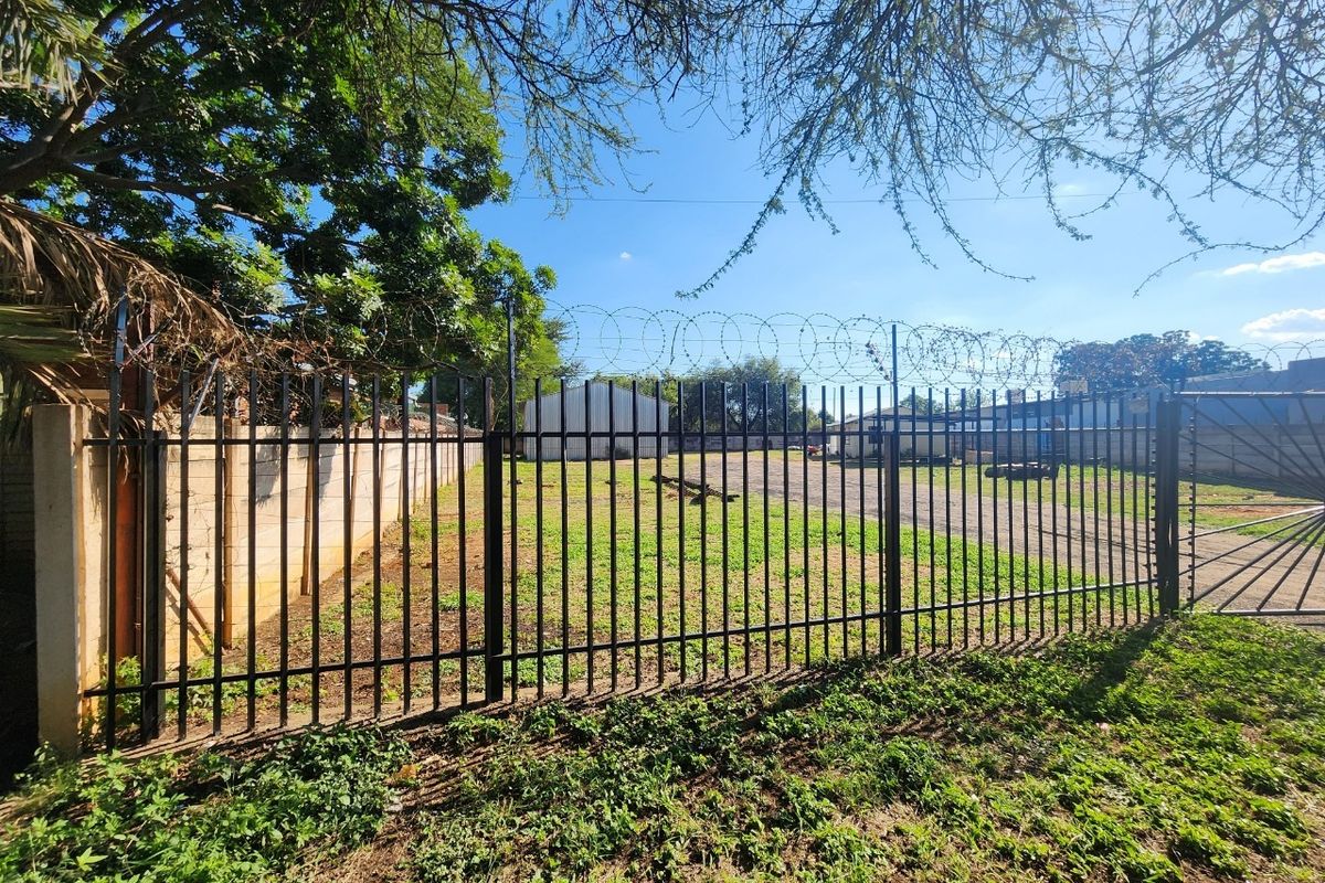 A secure industrial yard featuring steel palisade fencing, razor wire security, and a concrete boundary wall, with an industrial shed visible in the background.