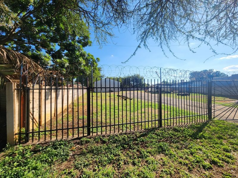 A secure industrial yard featuring steel palisade fencing, razor wire security, and a concrete boundary wall, with an industrial shed visible in the background.