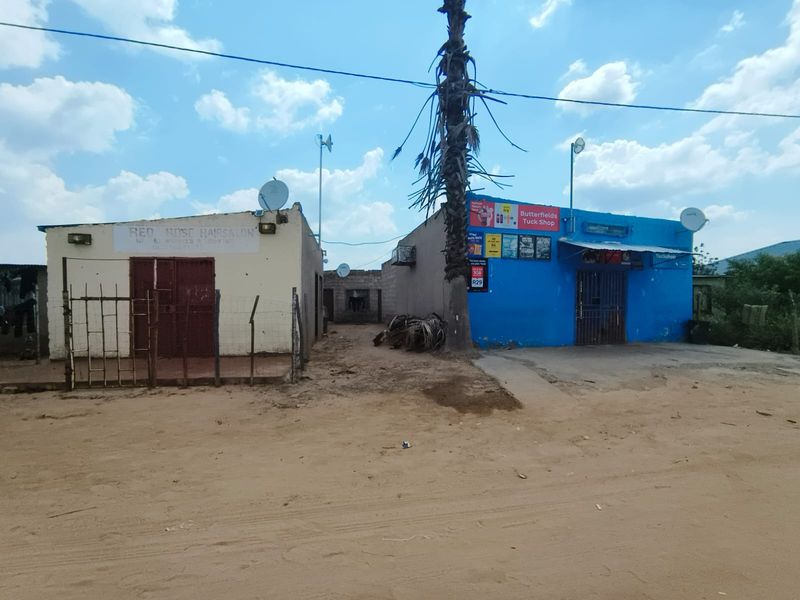 Street view of two adjacent commercial structures with metal security gates and satellite dishes, situated on an unpaved dirt lot.