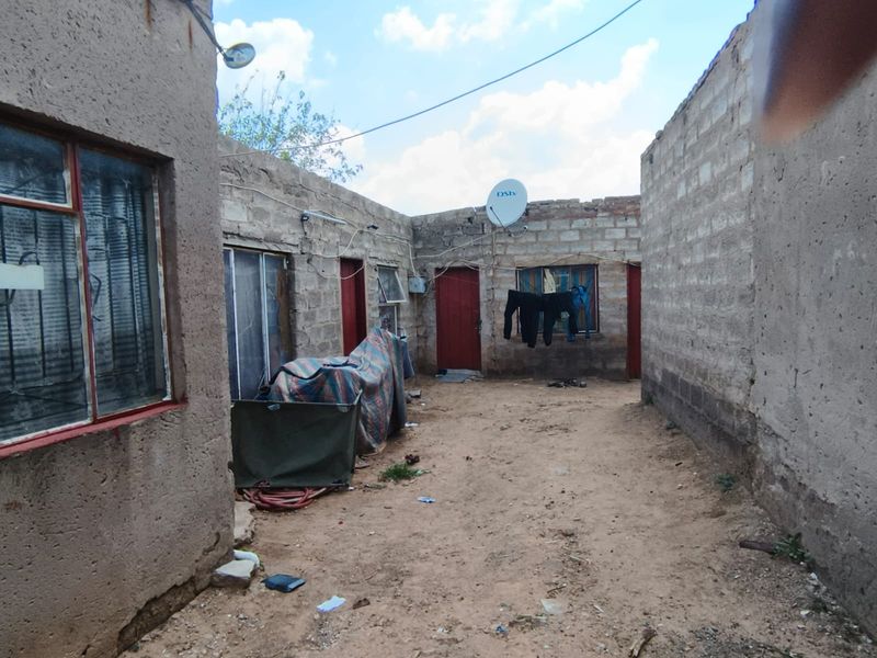 Rear courtyard area featuring exposed brick walls, multiple external access points, and unpaved ground, offering potential for landscaping and exterior improvement.