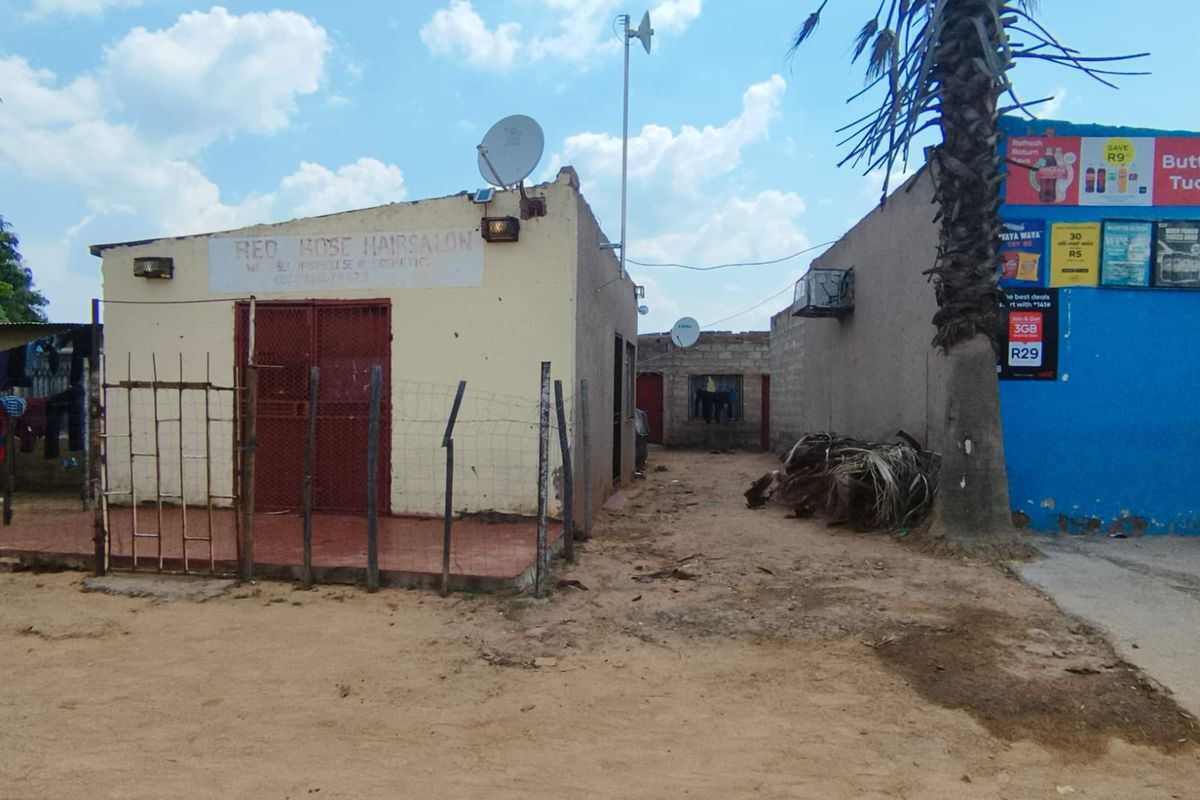 Exterior view of a commercial property featuring a security gate, satellite dish, and basic masonry construction with unpaved surrounding ground.