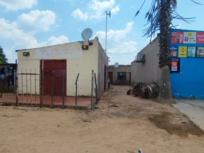 Exterior view of a commercial property featuring a security gate, satellite dish, and basic masonry construction with unpaved surrounding ground.