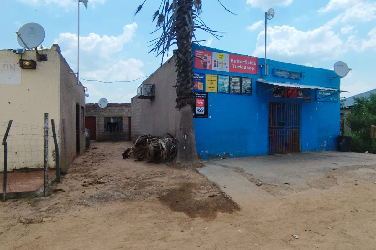 Exterior view of a commercial tuck shop building featuring blue painted walls, security gate, and external signage.