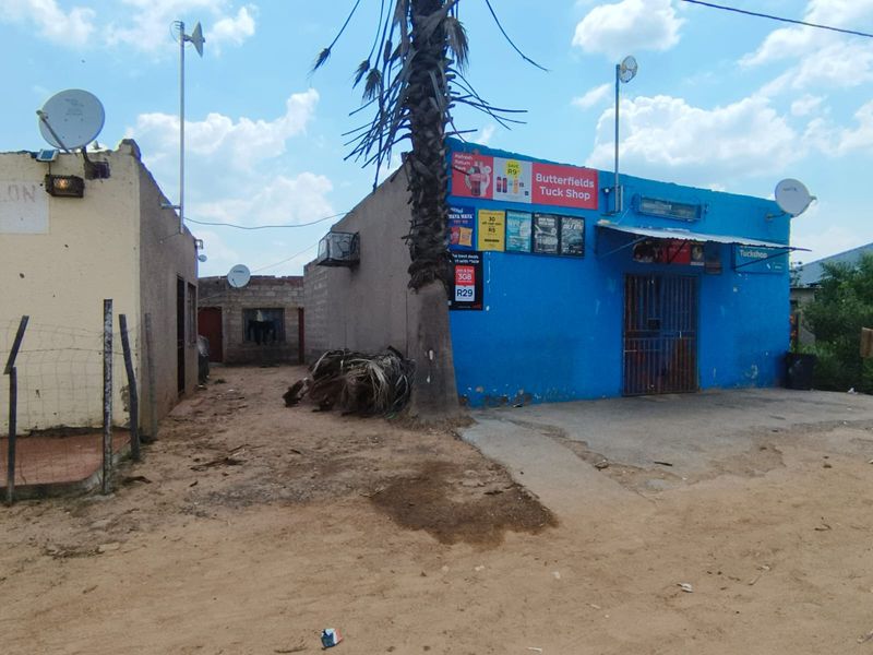 Exterior view of a commercial tuck shop building featuring blue painted walls, security gate, and external signage.