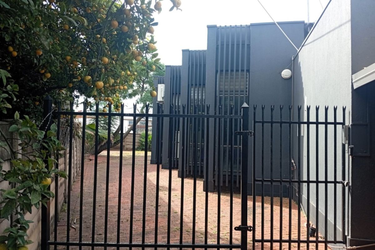 A secure rear exterior area featuring a metal gate, brick paving, and modern architectural vertical fins on the building facade.