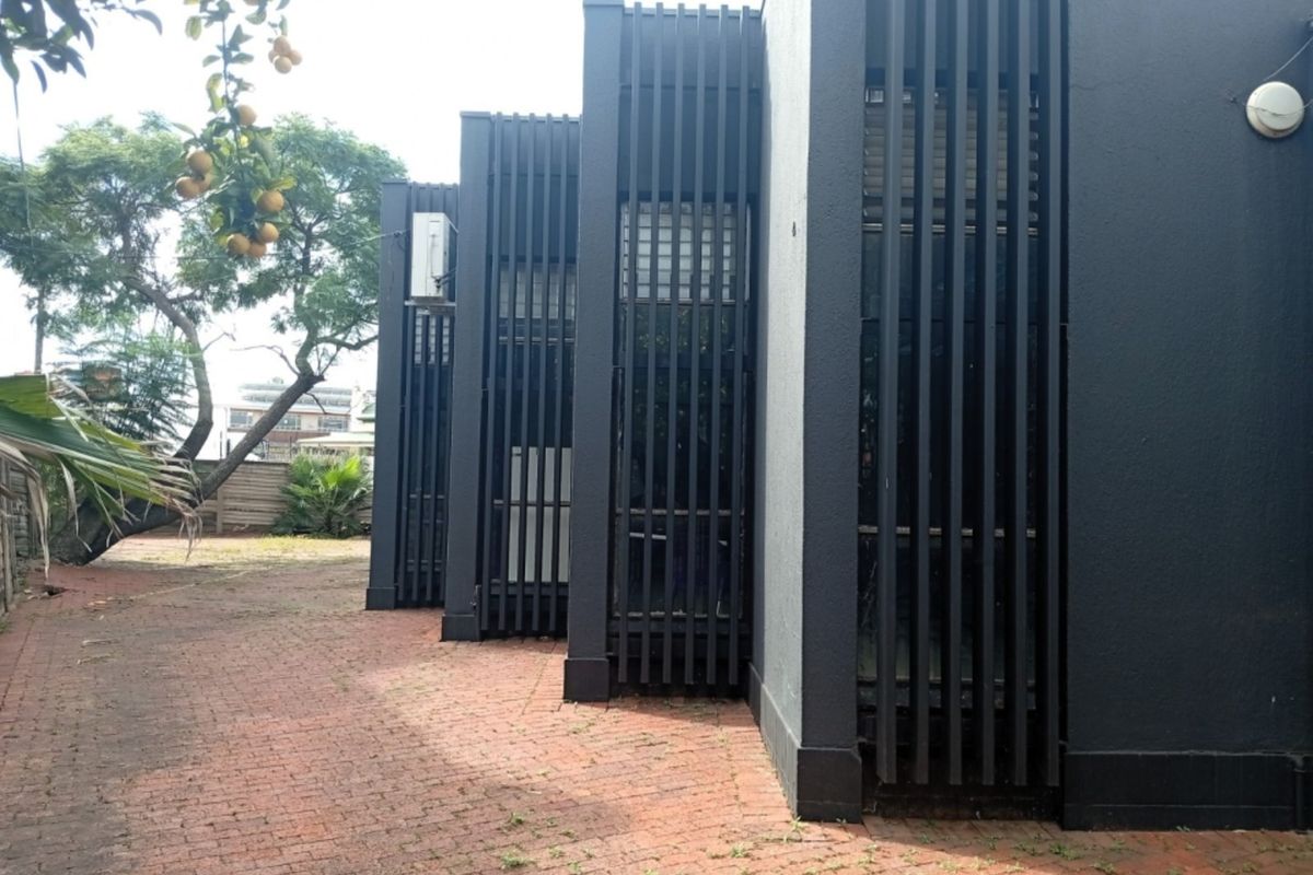Rear exterior view of the commercial property featuring modern vertical slat screening, a brick-paved courtyard area, and integrated exterior lighting.