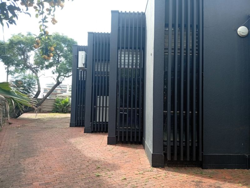 Rear exterior view of the commercial property featuring modern vertical slat screening, a brick-paved courtyard area, and integrated exterior lighting.