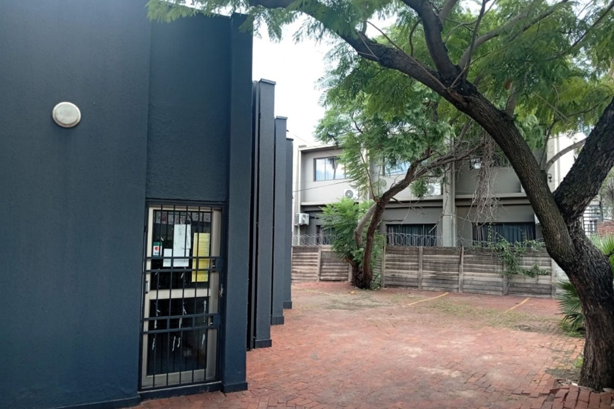 Rear exterior view of the commercial property featuring a paved courtyard, security gate, and perimeter walling with security fencing.