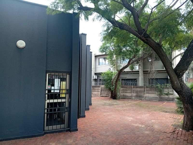 Rear exterior view of the commercial property featuring a paved courtyard, security gate, and perimeter walling with security fencing.