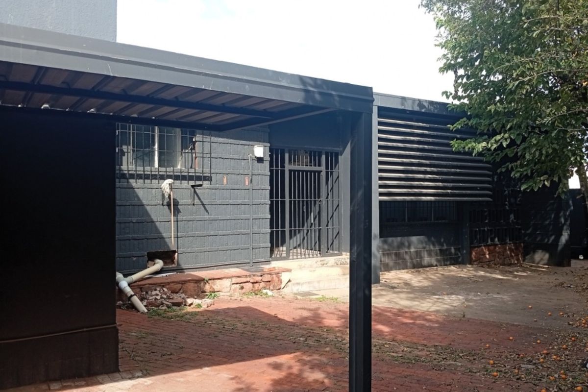 Rear exterior view of the commercial property featuring a carport, security bars on windows, and brick paved courtyard area.