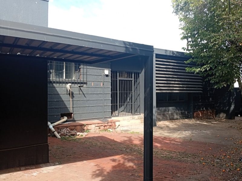Rear exterior view of the commercial property featuring a carport, security bars on windows, and brick paved courtyard area.