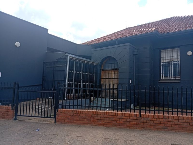 Front exterior view of a commercial building featuring a dark painted facade, tiled roof, and secure perimeter fencing with a gated entrance.