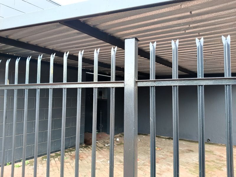 A secure, covered parking area featuring steel palisade fencing, a corrugated metal roof, and paved flooring.