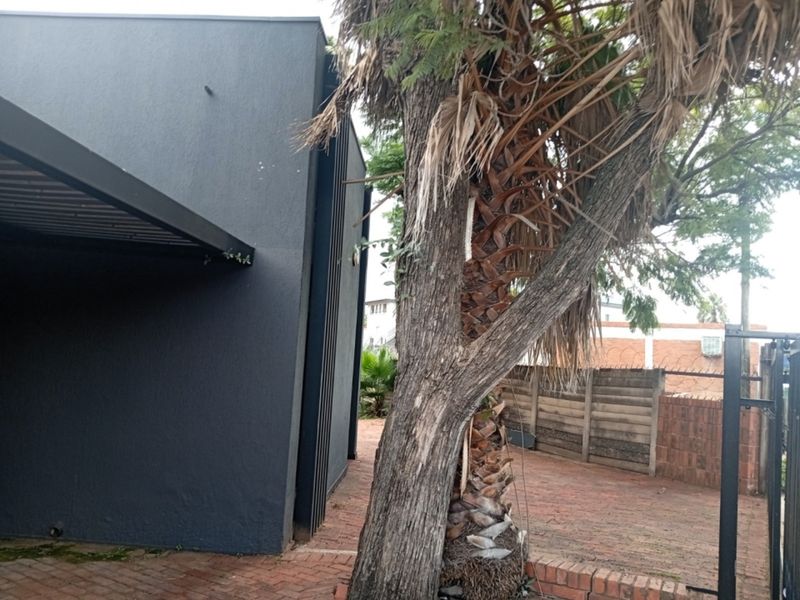 Rear exterior area featuring brick paving, a metal awning, and a perimeter wall with security spikes.