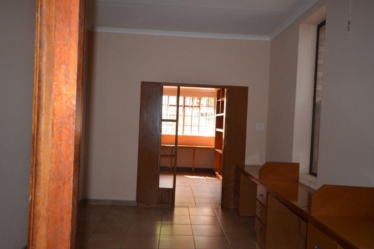 An empty office space featuring built-in wooden desks, tiled flooring, and a connecting doorway leading to an adjacent room with natural light.