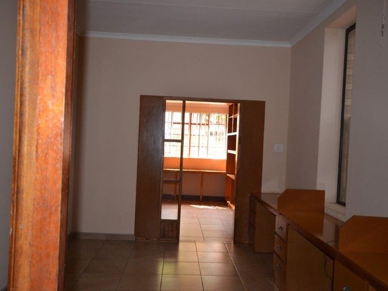 An empty office space featuring built-in wooden desks, tiled flooring, and a connecting doorway leading to an adjacent room with natural light.