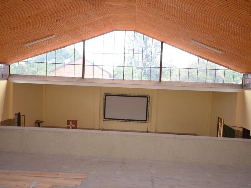 Spacious cinema room featuring a high timber-clad vaulted ceiling, large clerestory windows for natural light, and a built-in projector screen on a mezzanine level.