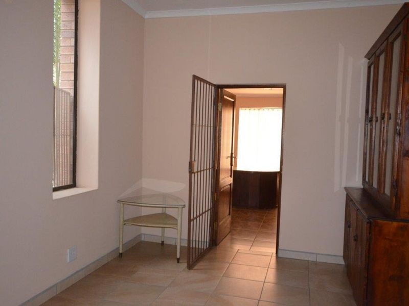 A living area featuring tiled flooring, coving, and a security gate leading to an adjacent room with natural light.