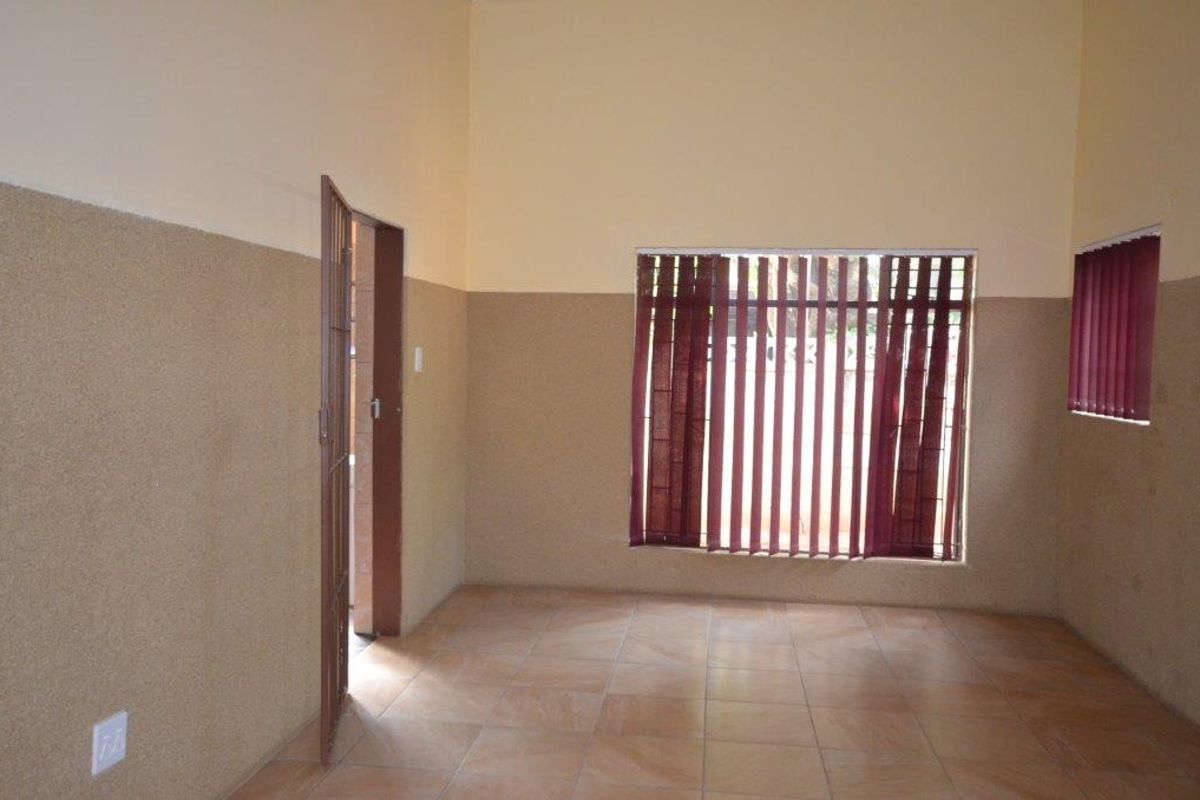 An empty, neutrally painted living area featuring tiled flooring, textured wall finishes, and security-fitted windows with vertical blinds.
