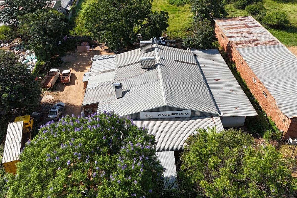Aerial view of an industrial depot facility featuring a large corrugated metal roof, solar water heating units, and surrounding yard space.