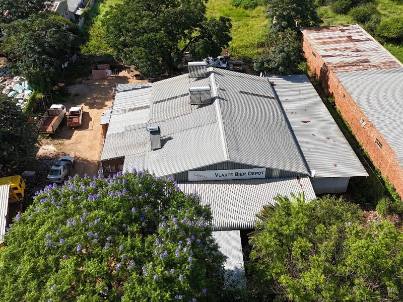 Aerial view of an industrial depot facility featuring a large corrugated metal roof, solar water heating units, and surrounding yard space.