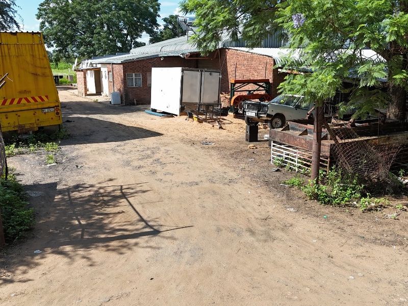 Rear exterior view of an industrial brick building with a corrugated metal roof and solar water heater, featuring an unpaved yard area.