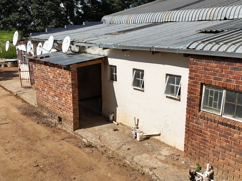 Rear exterior view of an industrial building featuring a corrugated metal roof, face brick and plastered masonry walls, and exposed utility plumbing.