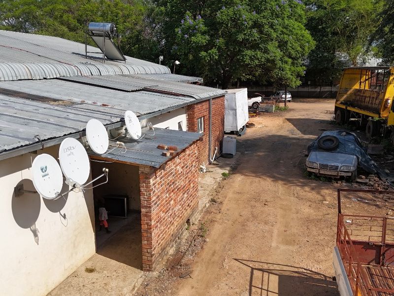 Rear exterior view of an industrial building featuring a corrugated metal roof, solar water heating system, and multiple satellite dishes.