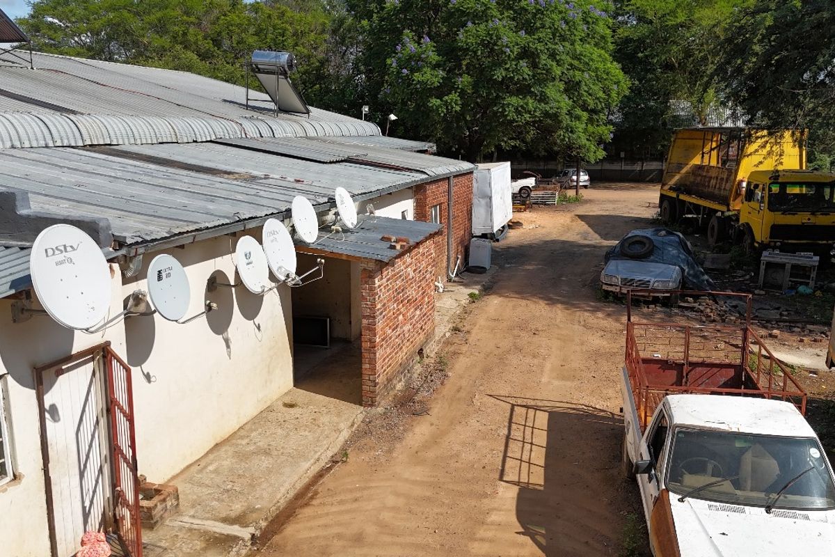 Aerial view of the rear industrial building exterior featuring a corrugated metal roof, solar water heater, and multiple satellite dishes mounted on the wall.